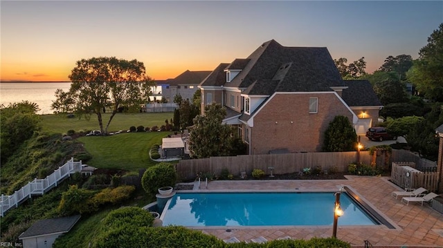 pool at dusk featuring a patio, a fenced in pool, a water view, and a fenced backyard