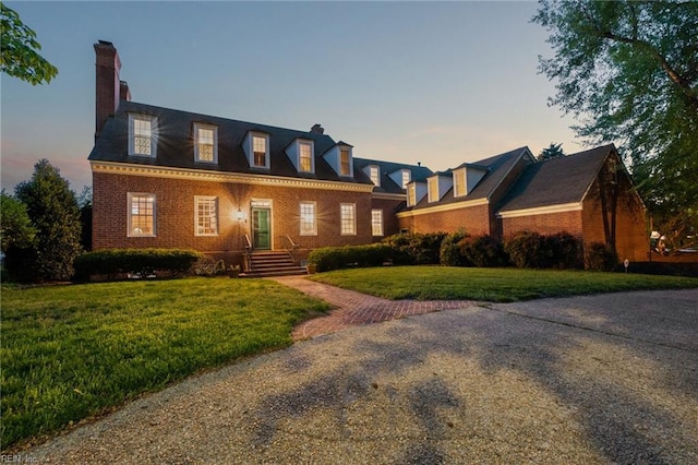 new england style home featuring a chimney, a front yard, and brick siding