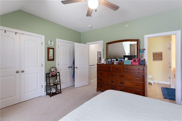 bedroom with multiple closets, ensuite bathroom, a ceiling fan, carpet, and vaulted ceiling