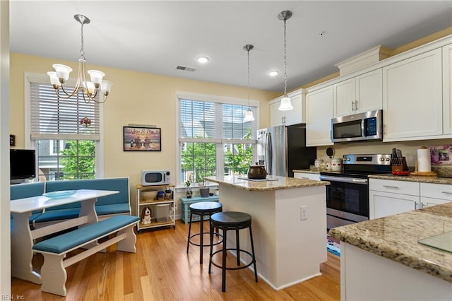 kitchen featuring white cabinets, light wood-style floors, stainless steel appliances, a kitchen island, and visible vents