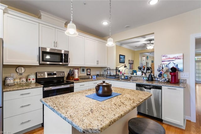 kitchen with decorative light fixtures, appliances with stainless steel finishes, a center island, a sink, and white cabinetry