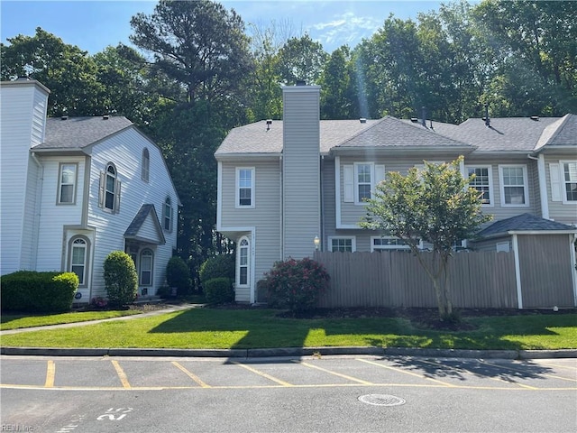 view of property featuring a front lawn, uncovered parking, fence, and a chimney