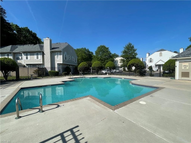 community pool with a patio, fence, and a residential view