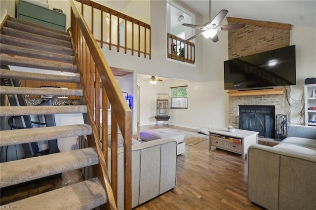 living room with stairway, ceiling fan, a brick fireplace, and wood finished floors