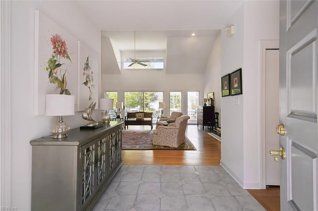 living room featuring a ceiling fan, a towering ceiling, baseboards, and light tile patterned flooring