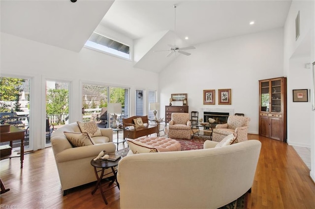 living room featuring high vaulted ceiling, ceiling fan, a glass covered fireplace, recessed lighting, and wood finished floors