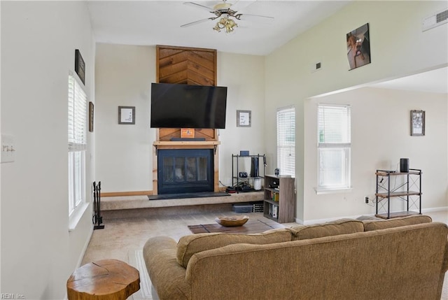 living room with a glass covered fireplace, baseboards, ceiling fan, and a high ceiling