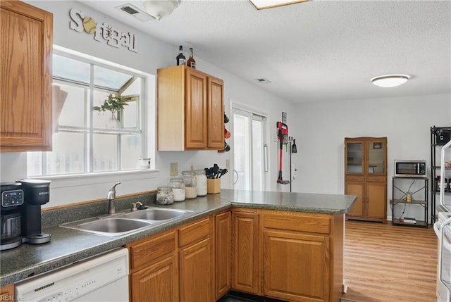 kitchen featuring dishwasher, a sink, a peninsula, stainless steel microwave, and dark countertops