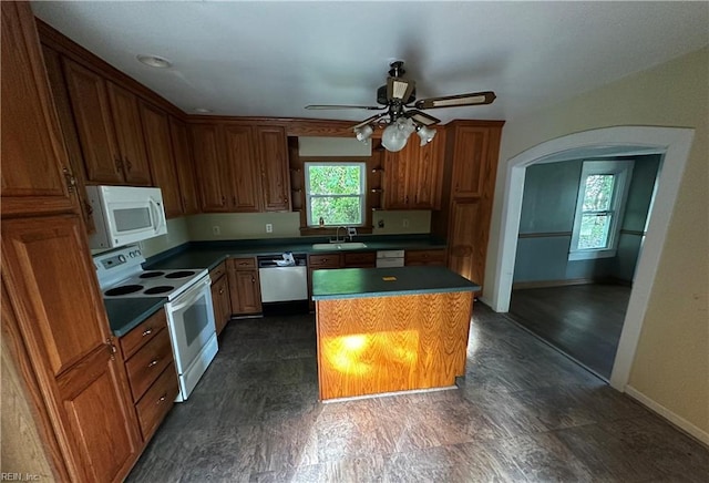 kitchen with ceiling fan, a sink, white appliances, arched walkways, and a kitchen island