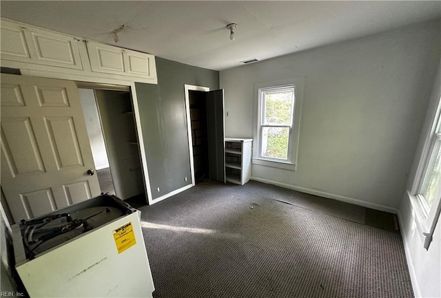 unfurnished bedroom with baseboards, dark carpet, and visible vents