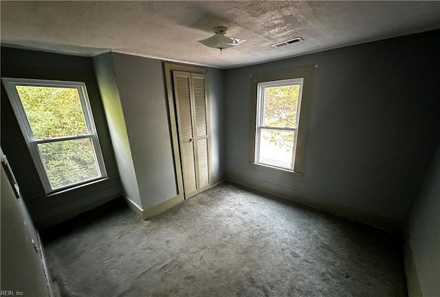 unfurnished bedroom with a textured ceiling, visible vents, baseboards, a closet, and carpet