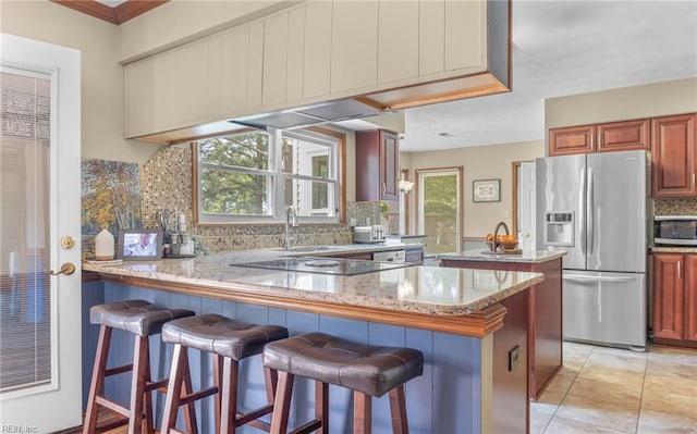 kitchen with decorative backsplash, appliances with stainless steel finishes, a sink, light stone counters, and a peninsula