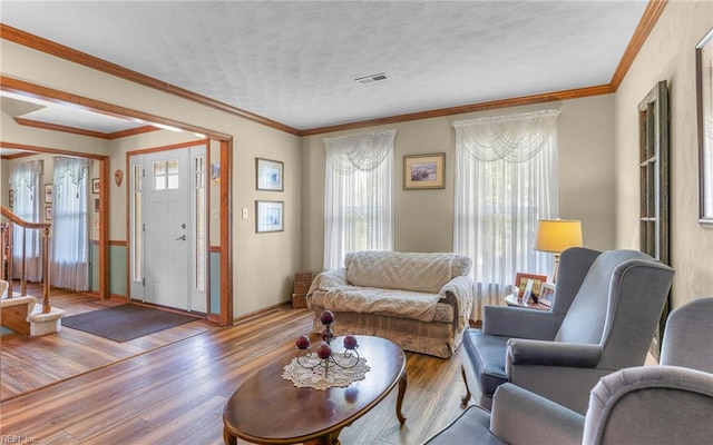 living area with visible vents, crown molding, wood finished floors, baseboards, and stairway