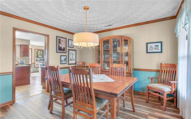 dining space with crown molding, baseboards, and light wood-style flooring