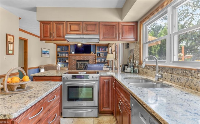 kitchen featuring light stone countertops, a fireplace, a sink, light tile patterned floors, and stainless steel appliances
