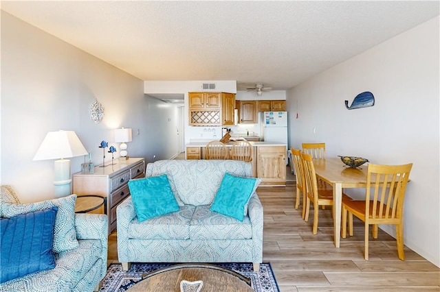 living area featuring a ceiling fan, light wood-type flooring, a textured ceiling, and visible vents