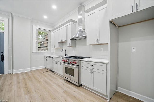 kitchen featuring crown molding, a sink, light countertops, stainless steel appliances, and wall chimney exhaust hood