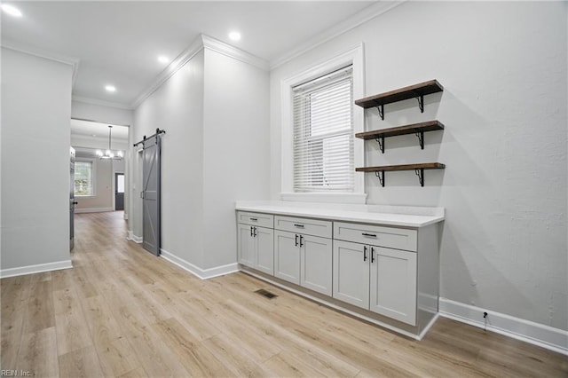 corridor with a barn door, visible vents, ornamental molding, and light wood-type flooring