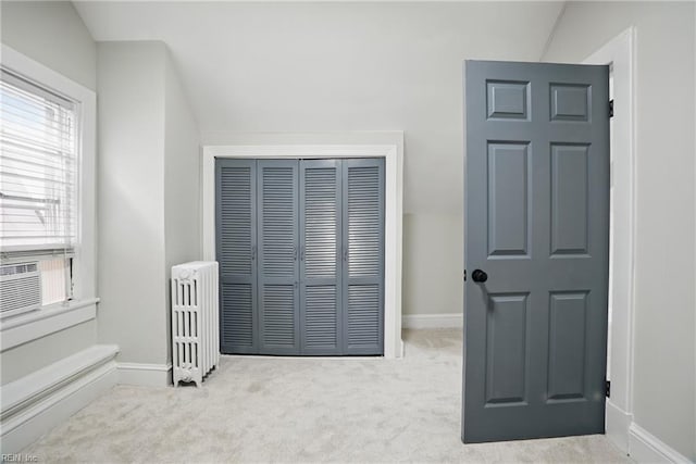 unfurnished bedroom featuring vaulted ceiling, baseboards, carpet floors, a closet, and radiator