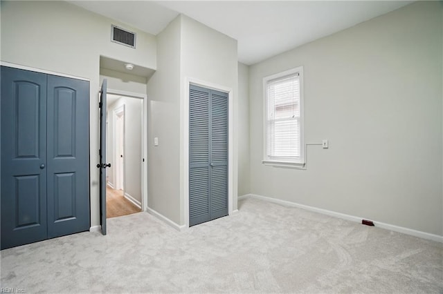 unfurnished bedroom featuring visible vents, baseboards, carpet floors, and two closets
