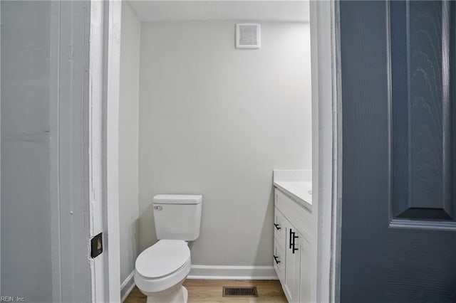 half bath featuring vanity, baseboards, toilet, and visible vents