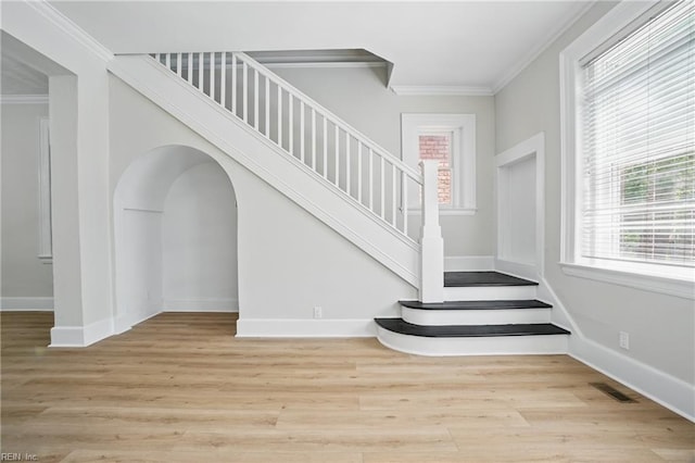 stairway featuring crown molding, baseboards, wood finished floors, and a wealth of natural light