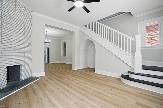unfurnished living room with a brick fireplace, ornamental molding, wood finished floors, and ceiling fan with notable chandelier
