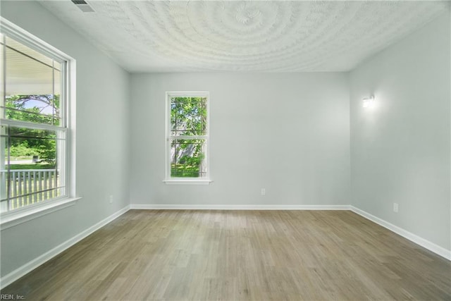 unfurnished room with a textured ceiling, baseboards, plenty of natural light, and wood finished floors