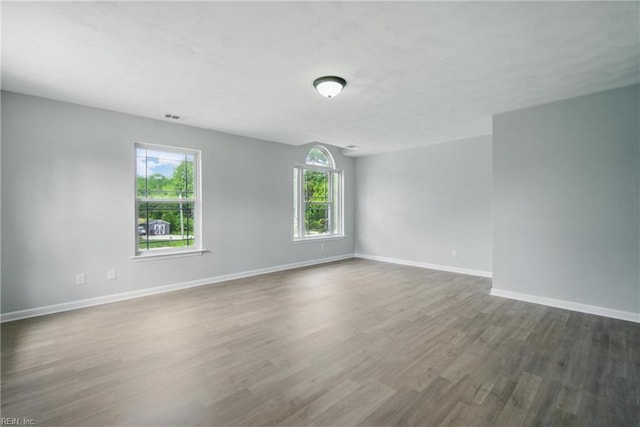unfurnished room featuring baseboards, visible vents, dark wood finished floors, and a wealth of natural light
