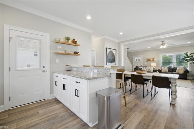 kitchen featuring ornamental molding, a peninsula, light stone countertops, light wood-type flooring, and white cabinetry