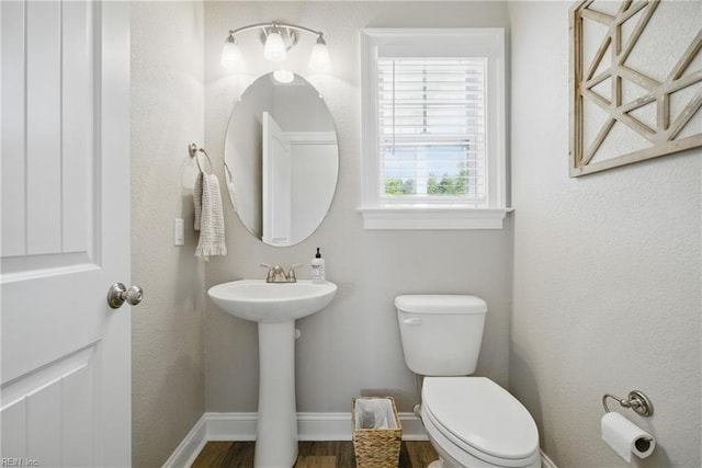 half bathroom featuring a sink, baseboards, toilet, and wood finished floors