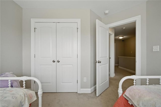 bedroom with baseboards, light colored carpet, and a closet