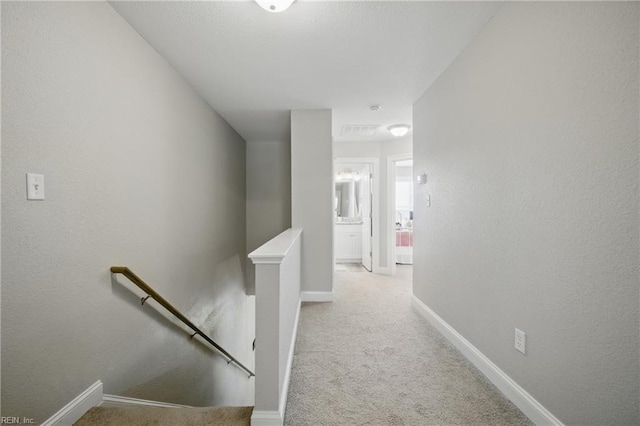 hall featuring light colored carpet, baseboards, visible vents, and an upstairs landing