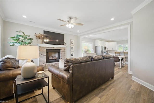 living room with a brick fireplace, a ceiling fan, recessed lighting, and light wood-style floors