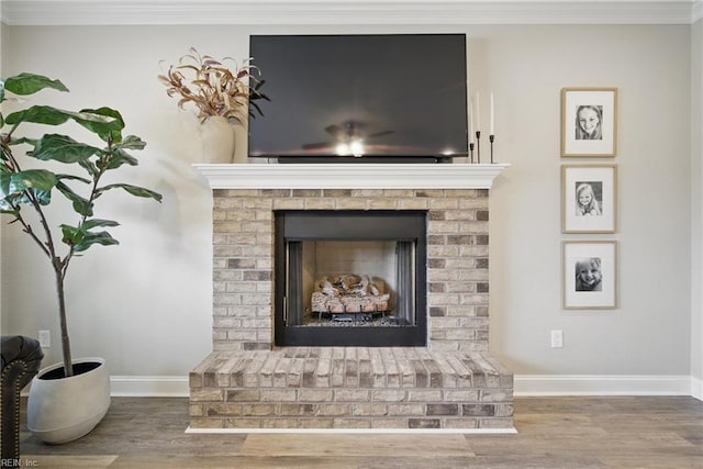 room details with crown molding, baseboards, a brick fireplace, and wood finished floors