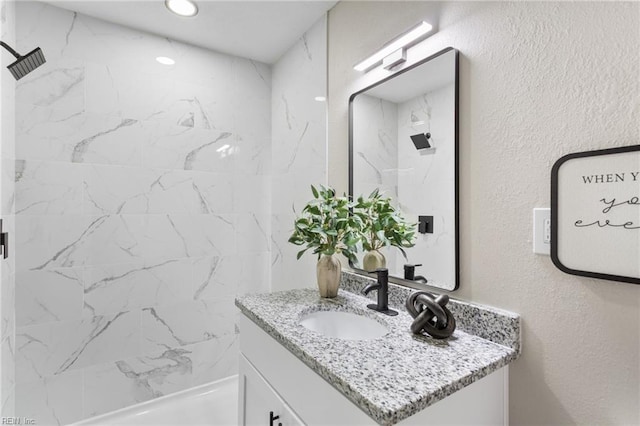 bathroom featuring vanity, a marble finish shower, and a textured wall
