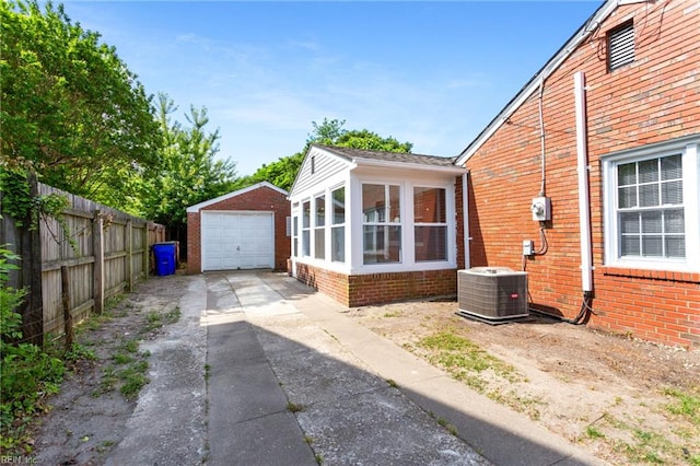 view of side of home with driveway, central air condition unit, brick siding, a detached garage, and fence