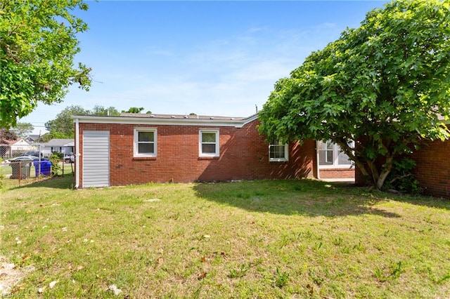 back of property with brick siding, a lawn, and fence