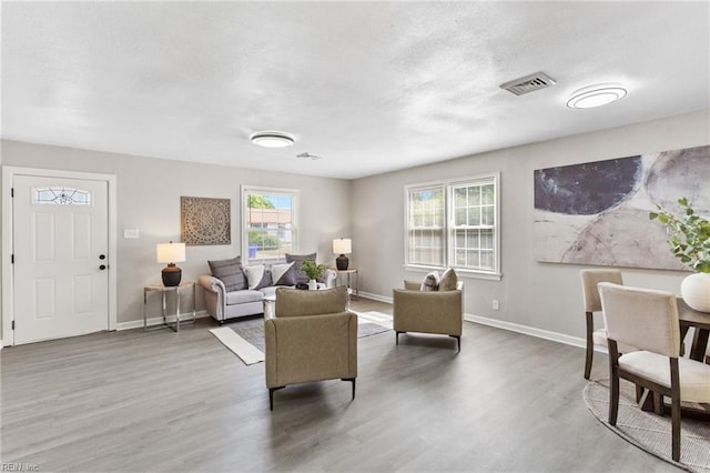 living area featuring a textured ceiling, baseboards, visible vents, and wood finished floors