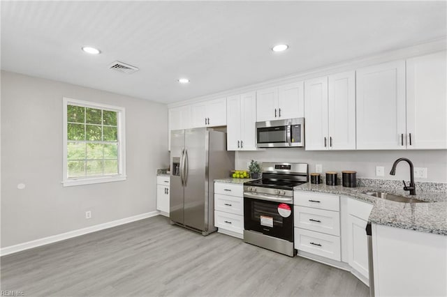 kitchen with a sink, light wood finished floors, stainless steel appliances, white cabinetry, and visible vents