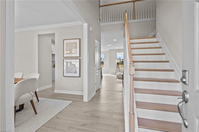 foyer entrance with baseboards, crown molding, wood finished floors, and stairway