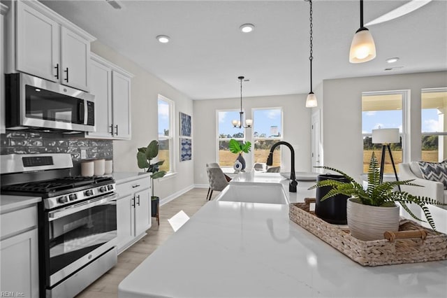 kitchen with baseboards, white cabinets, appliances with stainless steel finishes, a notable chandelier, and hanging light fixtures
