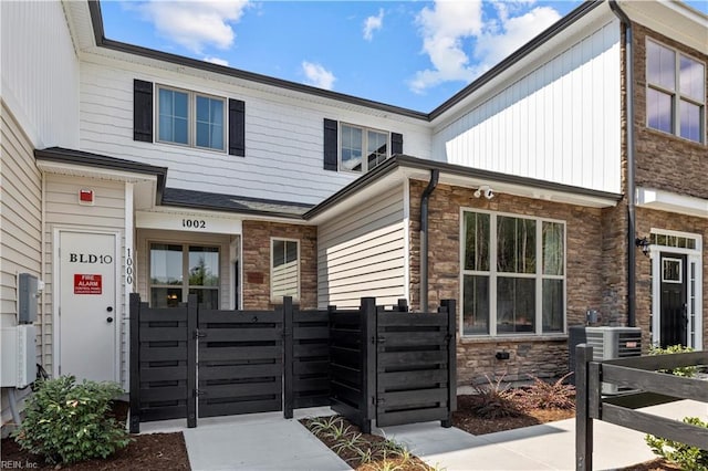view of front of house featuring board and batten siding, fence private yard, a gate, central AC, and stone siding