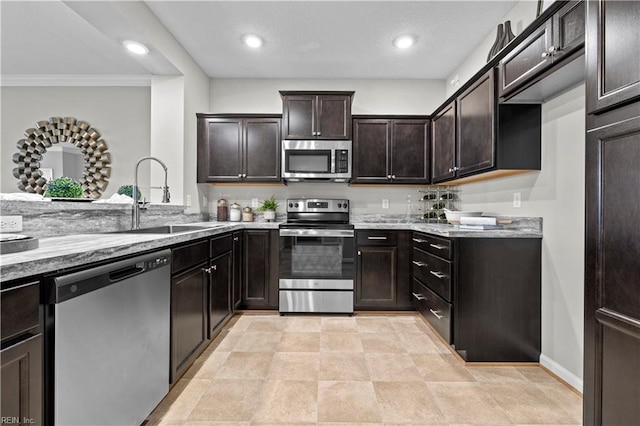 kitchen with ornamental molding, dark brown cabinets, light stone counters, a sink, and stainless steel appliances