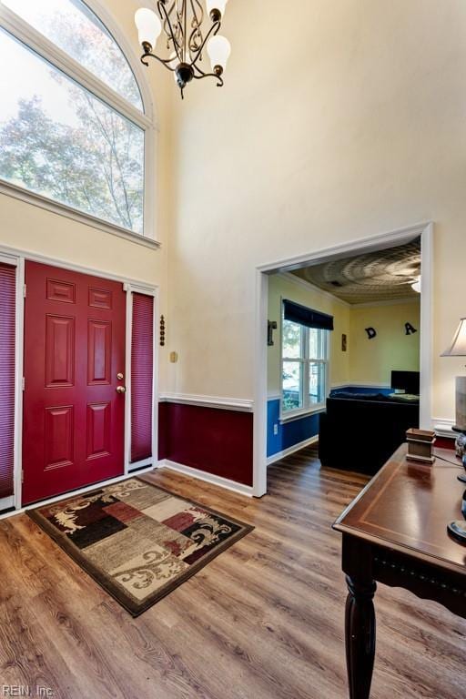 foyer with an inviting chandelier, a high ceiling, wood finished floors, and crown molding