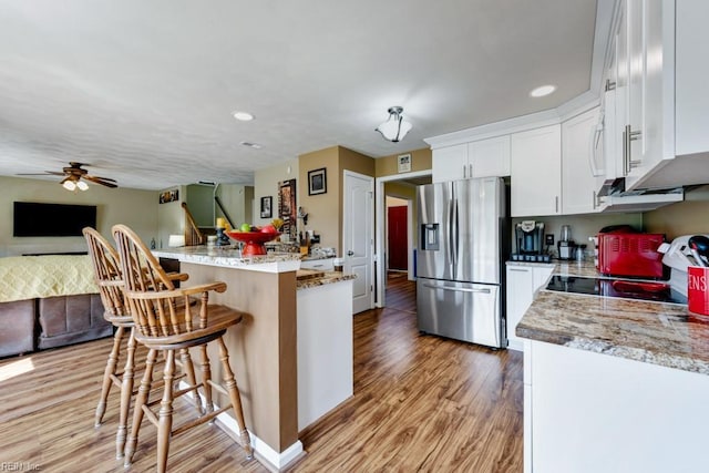 kitchen with stainless steel fridge with ice dispenser, a kitchen bar, light wood-style flooring, and open floor plan