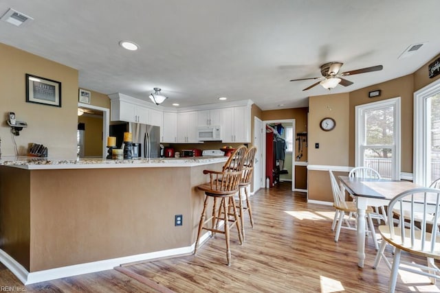 kitchen with visible vents, white microwave, light wood-type flooring, stainless steel fridge with ice dispenser, and a ceiling fan