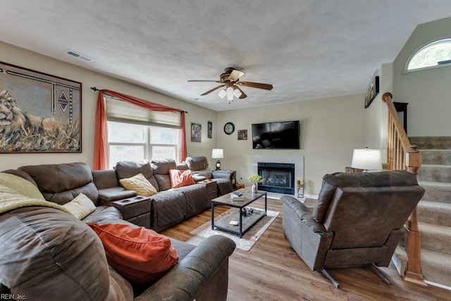 living room with ceiling fan, visible vents, wood finished floors, and a fireplace