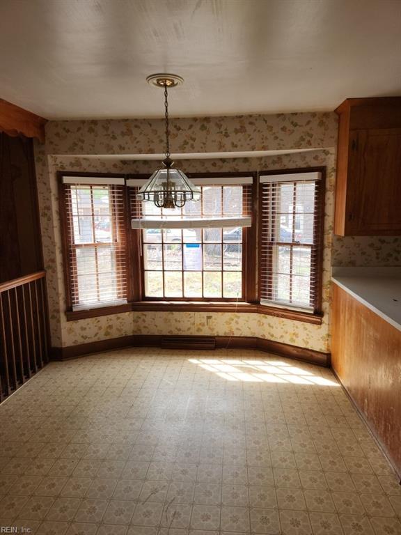 unfurnished dining area featuring an inviting chandelier, baseboards, and wallpapered walls