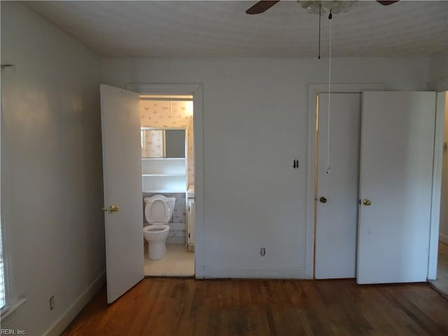 unfurnished bedroom featuring ensuite bathroom, baseboards, wood finished floors, and a closet